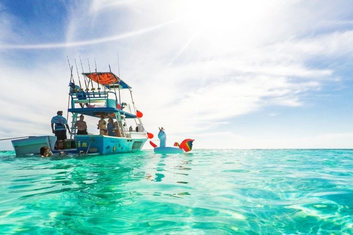 Boat on turquoise ocean with people and inflatable toy under a clear sky.