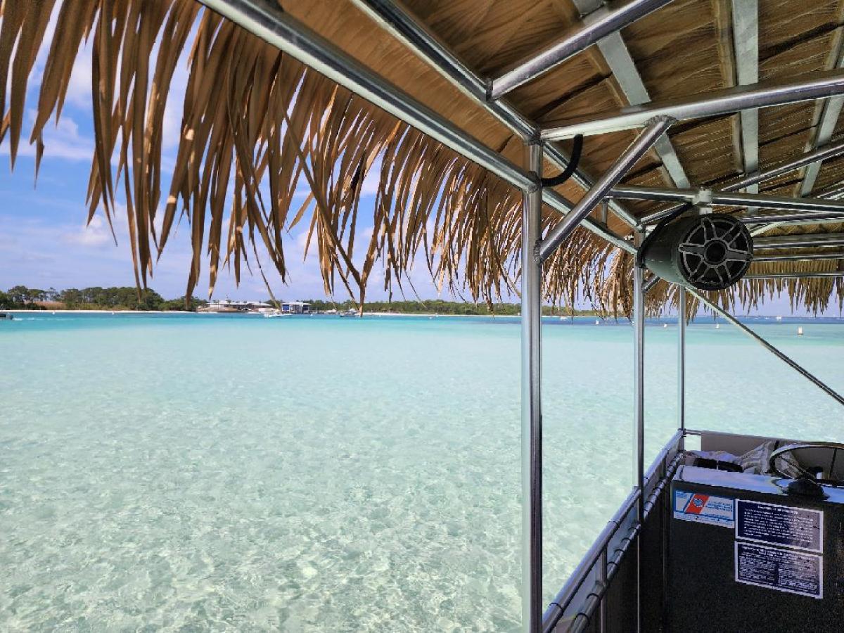 View from a thatched-roof boat over a clear, turquoise sea with a distant shoreline.