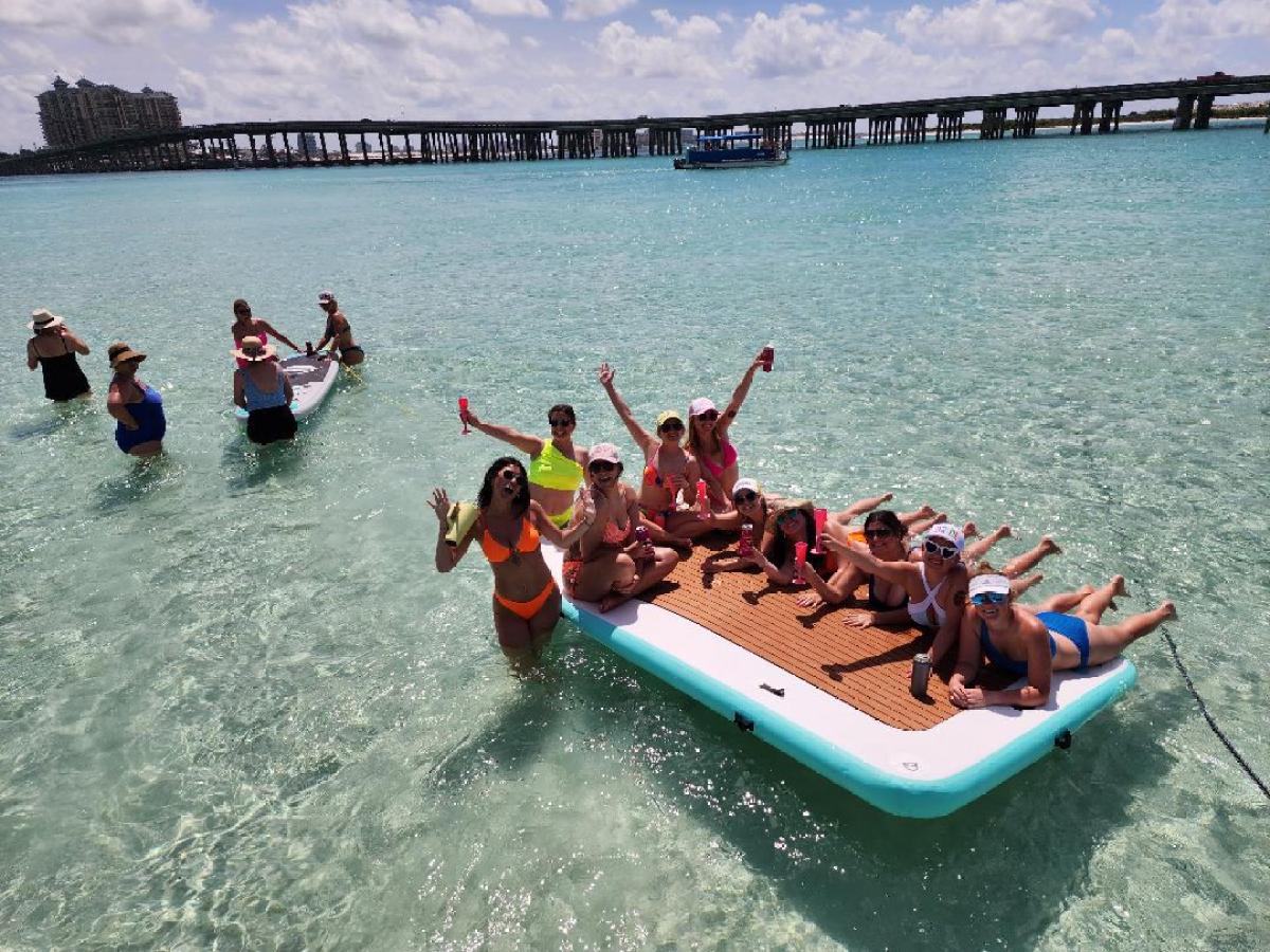 Group of people relaxing on a float in clear water near a bridge on a sunny day.