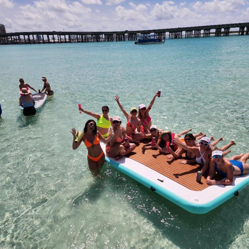 Group of people relaxing on a float in clear water near a bridge on a sunny day.