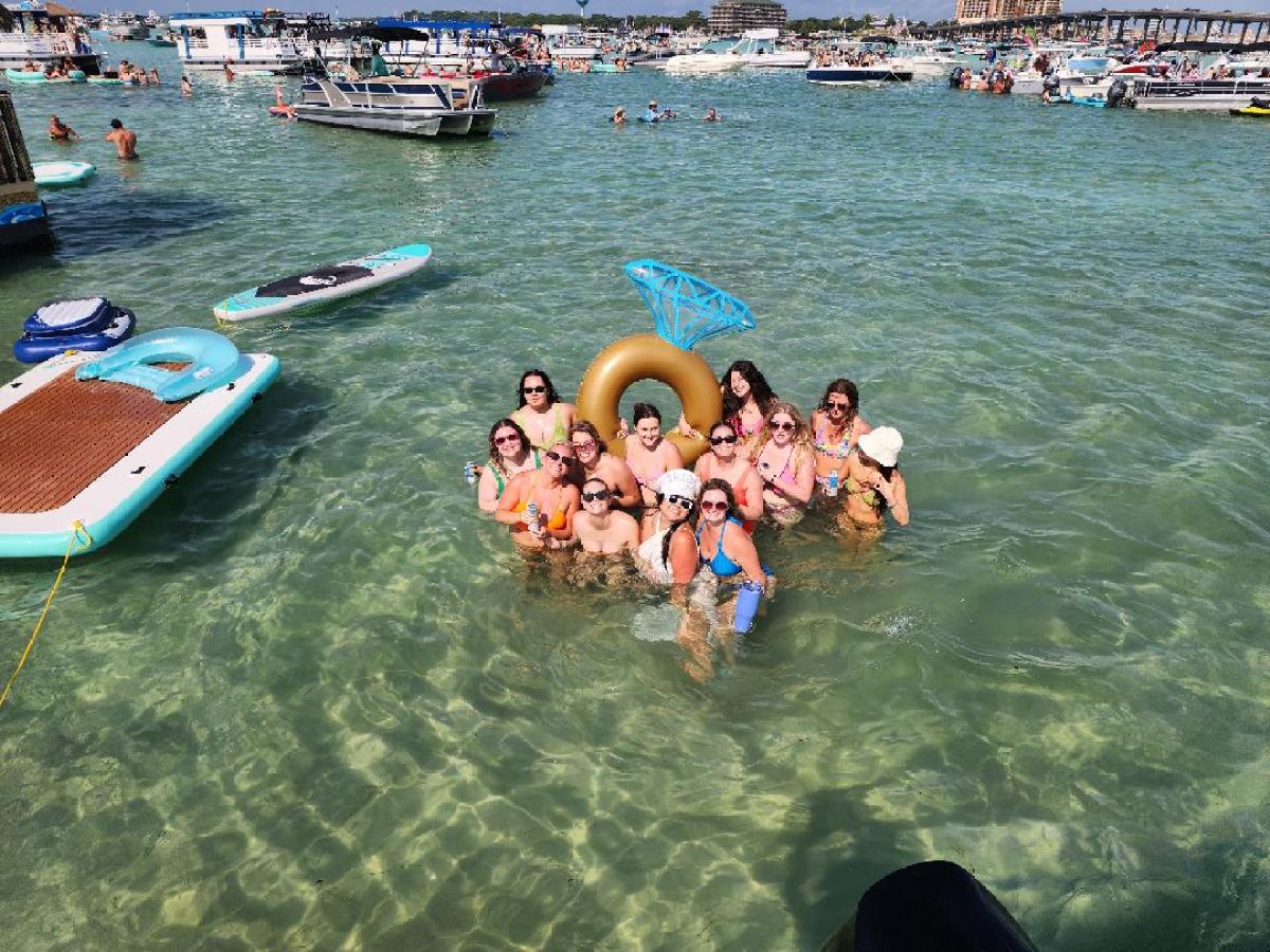Group of people in water with floating swim ring and paddleboards nearby, sunny day.