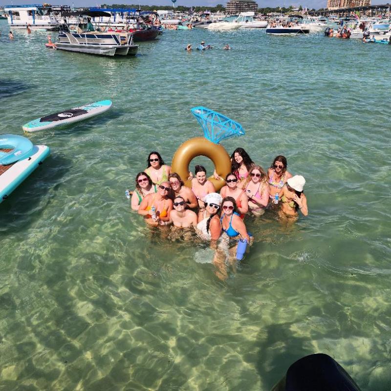 Group of people in water with floating swim ring and paddleboards nearby, sunny day.
