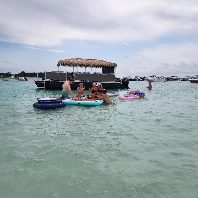 People relaxing on floating devices in clear water near a boat with a thatched roof.
