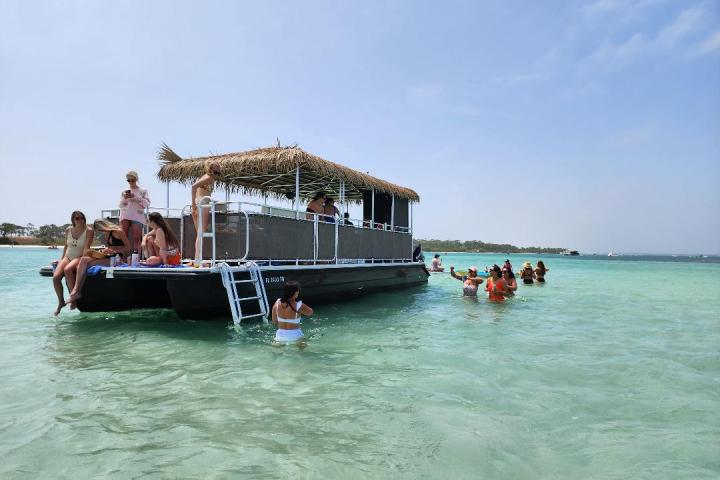 People on a floating barge in shallow, clear ocean water, with others swimming nearby, under a blue sky.