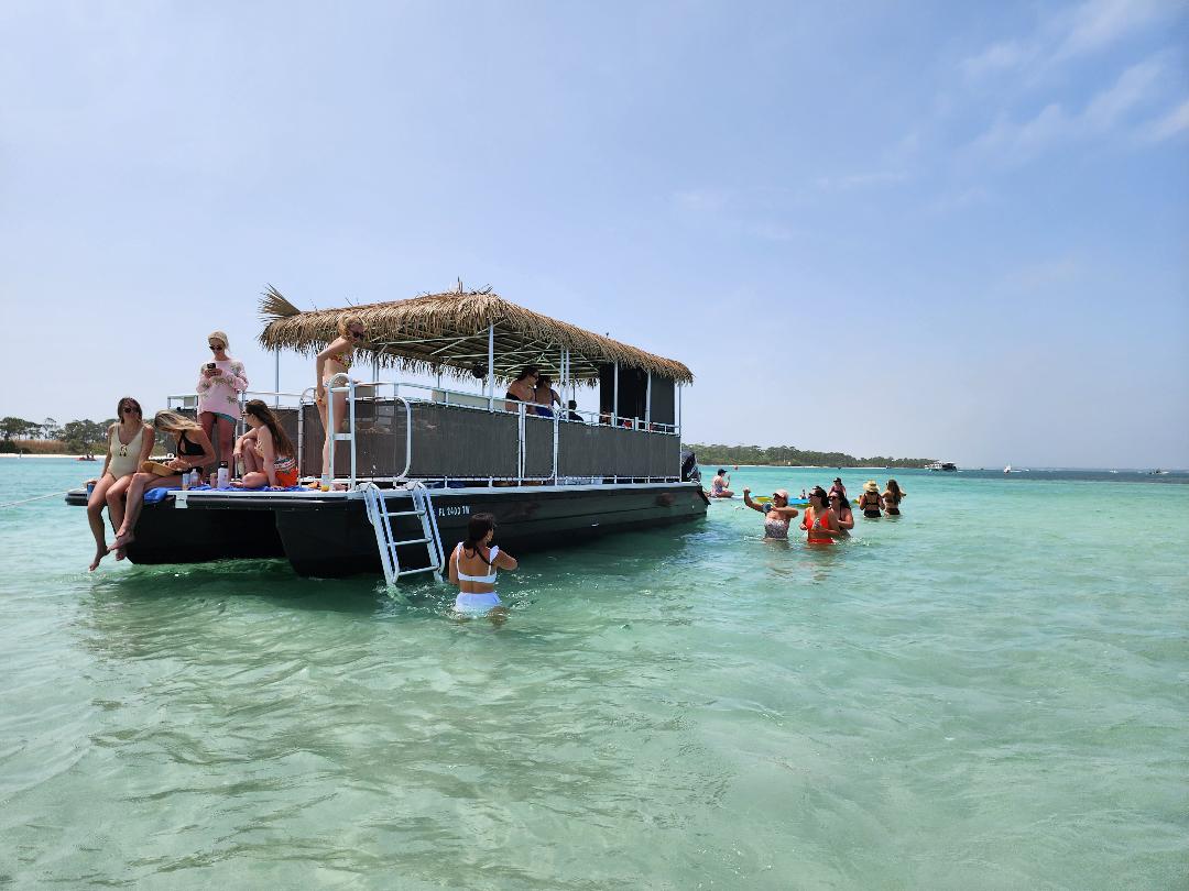 image 3 People on a floating barge in shallow, clear ocean water, with others swimming nearby, under a blue sky.