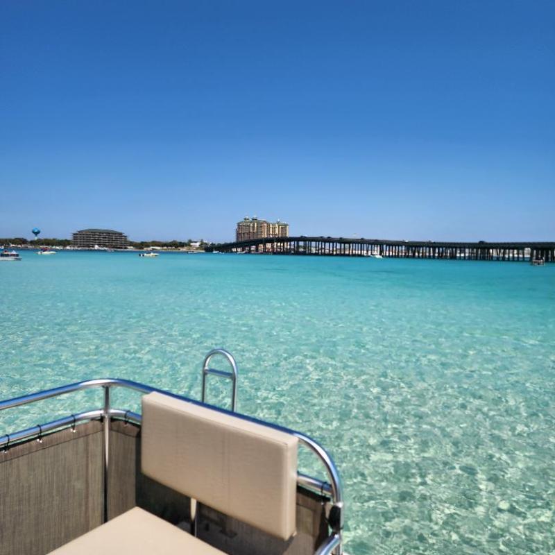 View from a boat on clear turquoise water with distant buildings and blue sky.